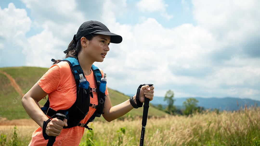 Trilha ativa de mulheres jovens atravessando um prado em uma trilha gramada no alto das montanhas à tarde com vara de trekking