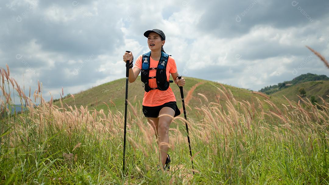 Trilha ativa de mulheres jovens atravessando um prado em uma trilha gramada no alto das montanhas à tarde com vara de trekking