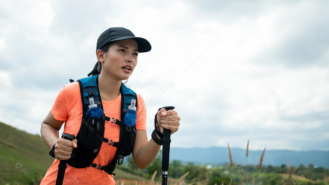 Trilha ativa de mulheres jovens atravessando um prado em uma trilha gramada no alto das montanhas à tarde com vara de trekking