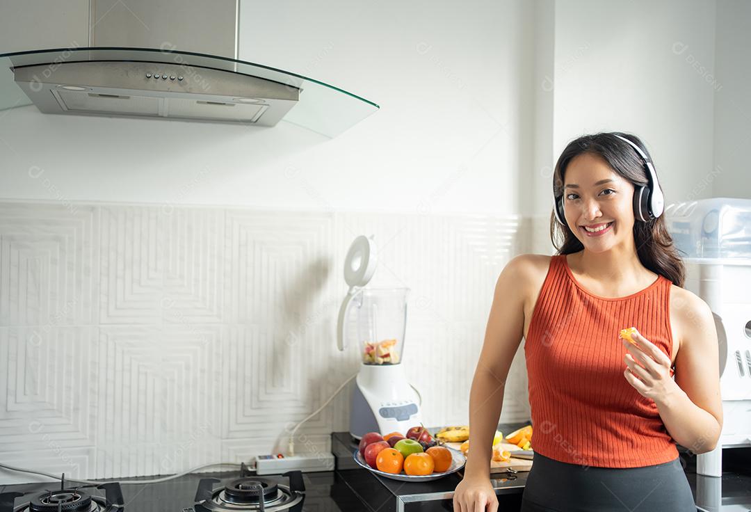 mulher ouvindo música através de fones de ouvido na cozinha em casa - conceitos de estilos de vida