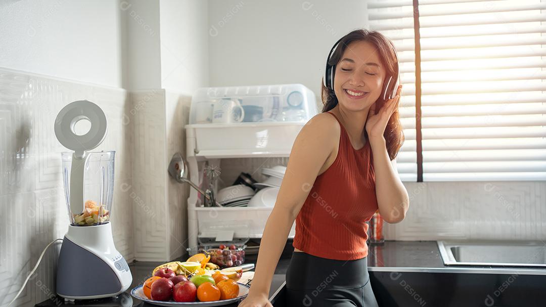 mulher ouvindo música através de fones de ouvido na cozinha em casa - conceitos de estilos de vida
