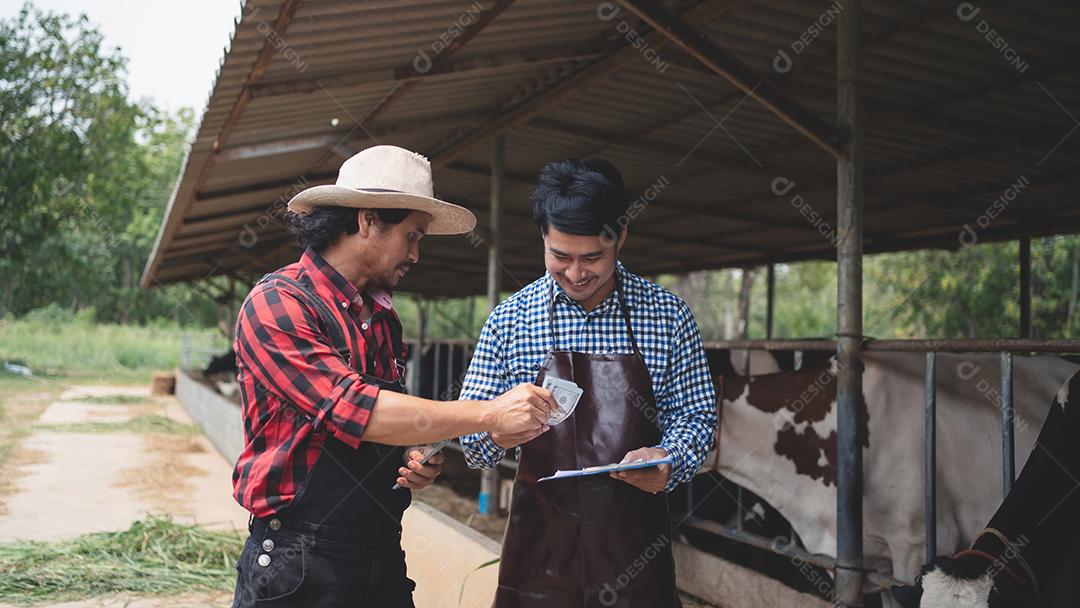Trabalhadores do sexo masculino pagam dinheiro e apertam as mãos dos agricultores na fazenda leiteira. Conceito de indústria agrícola, agricultura e pecuária, vaca na fazenda de gado leiteiro comendo feno. Estábulo, pequena empresa