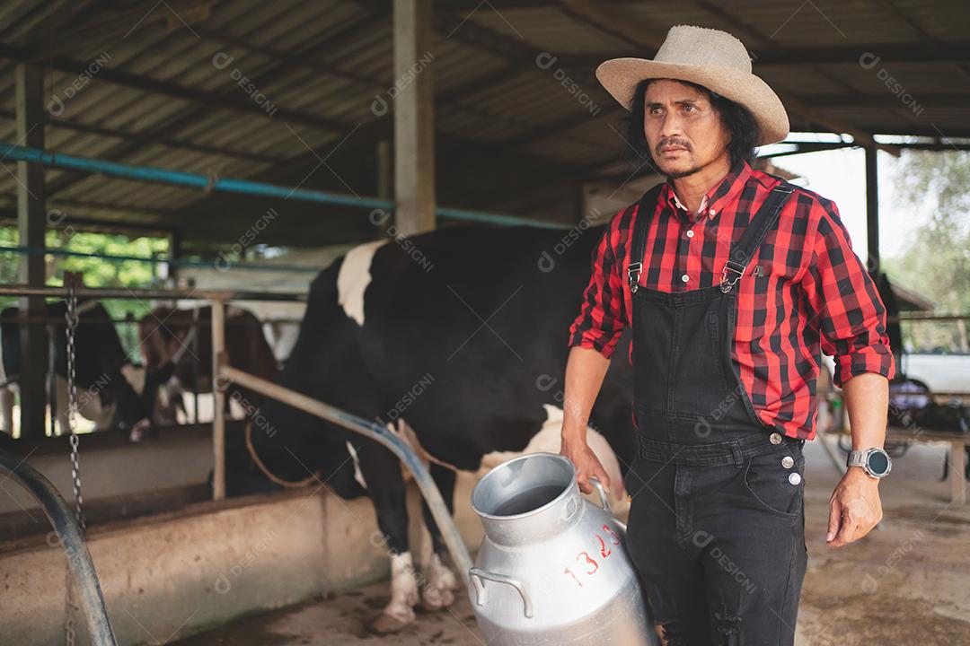 agricultor carregando um barril de leite passa pelo estábulo leiteiro., fazenda de vacas, pequenas empresas