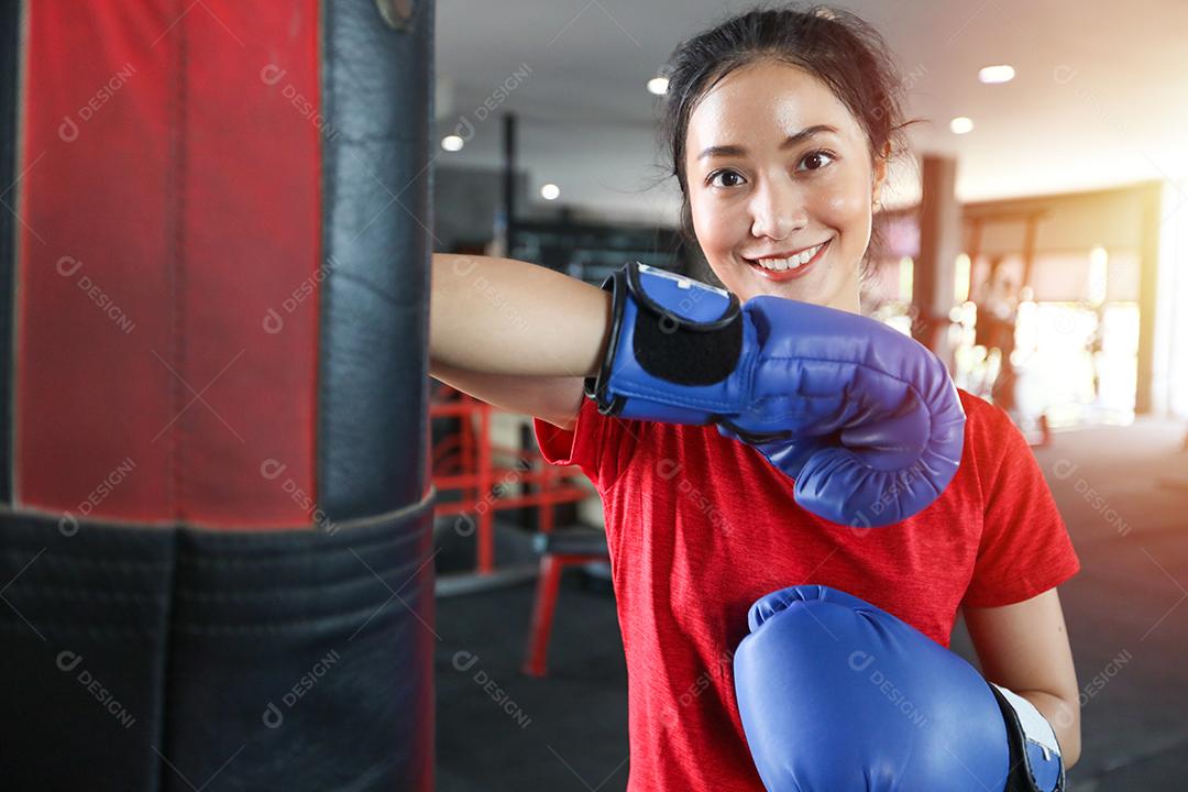 Mulheres bonitas boxeador asiático feliz e divertido fitness boxe e perfurando um saco com luvas de boxe vestindo.