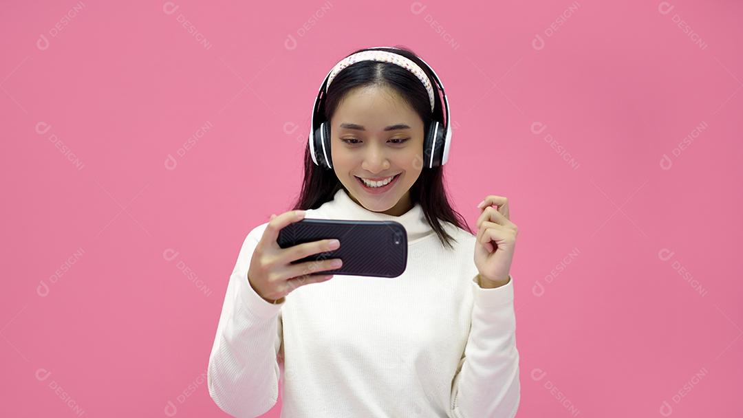 Mulheres asiáticas sorrindo e ouvindo e cantando a música com fones de ouvido em um estúdio rosa