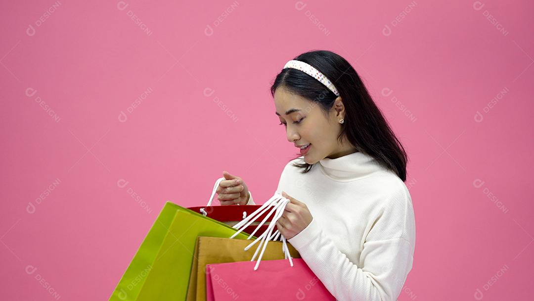 Mulher jovem feliz sorrindo e segurando sacolas de compras e cartão de crédito enquanto fazia algumas compras em um fundo de estúdio rosa