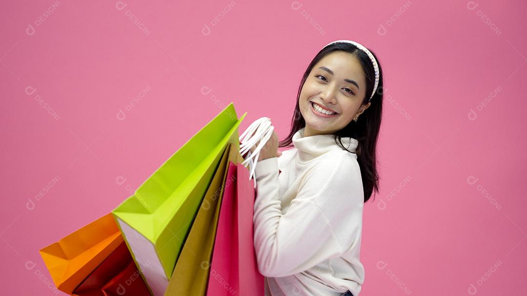 Mulher jovem feliz sorrindo e segurando sacolas de compras e cartão de crédito enquanto fazia algumas compras em um fundo de estúdio rosa