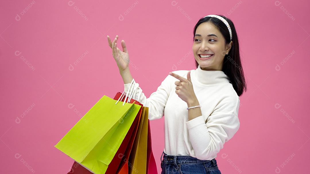 Mulher jovem feliz sorrindo e segurando sacolas de compras e cartão de crédito enquanto fazia algumas compras em um fundo de estúdio rosa