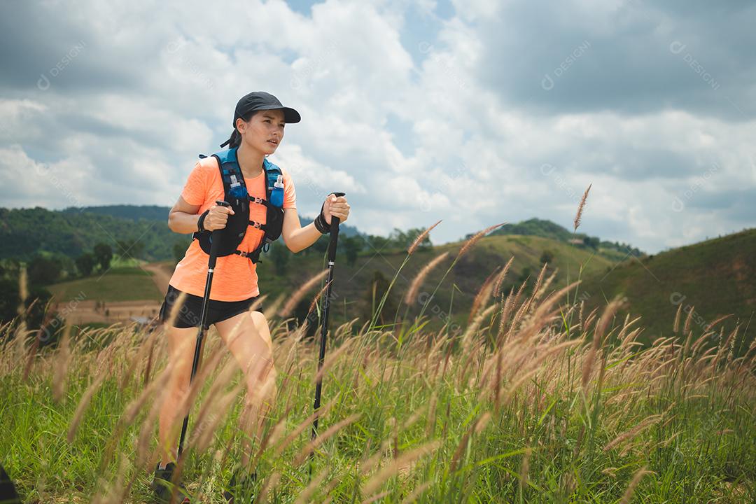Trilha ativa de mulheres jovens atravessando um prado em uma trilha gramada no alto das montanhas à tarde com vara de trekking