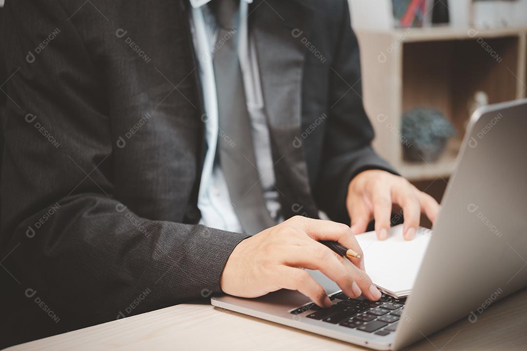 Pessoa de homem usando laptop de computador teclado segurando caneta e livro na mesa.