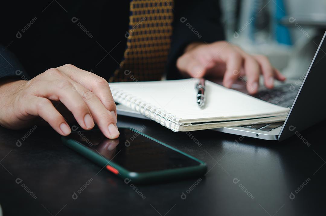 Empresário tocando rede de tecnologia de internet digital de telefone inteligente móvel com computador portátil e livro de caneta na mesa.