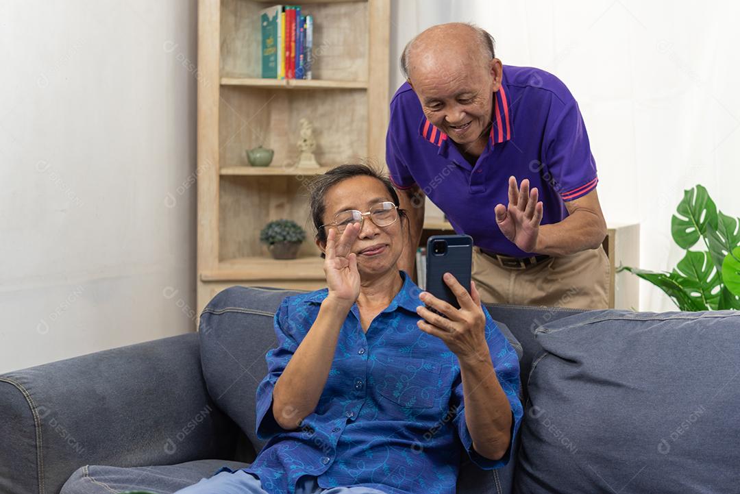 Senhor asiático segurando comunicação de telefone inteligente móvel chamada de vídeo online na internet juntos no sofá em casa.