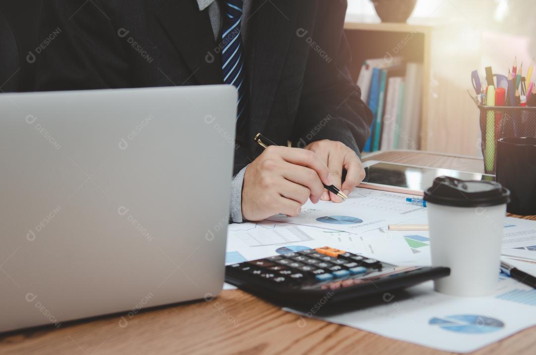 Empresário segurando o gráfico de documento de caneta contabilidade finanças papel análise gráfico investimento de marketing e economia de relatório com computador portátil na mesa no escritório.