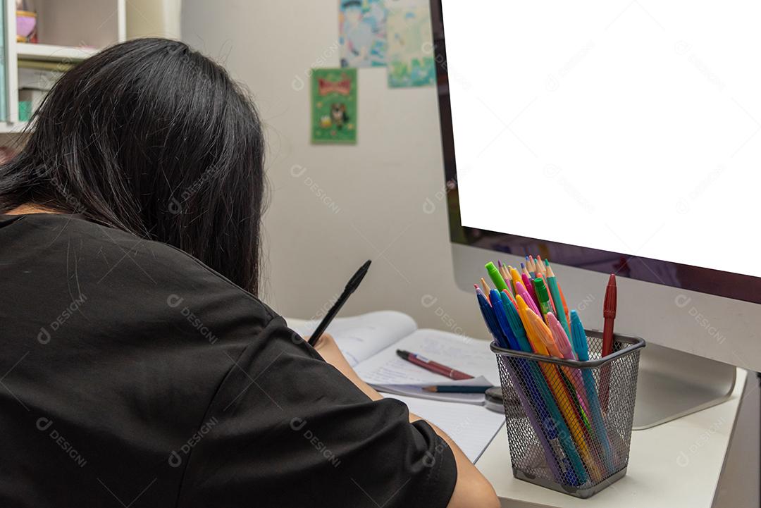 Aluna asiática está escrevendo lição de casa e lendo livro na mesa