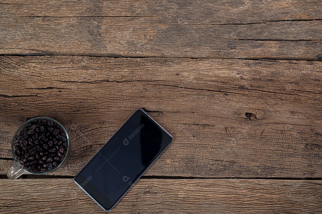 Grãos de café de telefones inteligentes deitados em uma vista superior de mesa de madeira