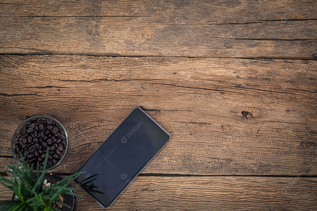 Grãos de café de telefones inteligentes deitados em uma vista superior de mesa de madeira