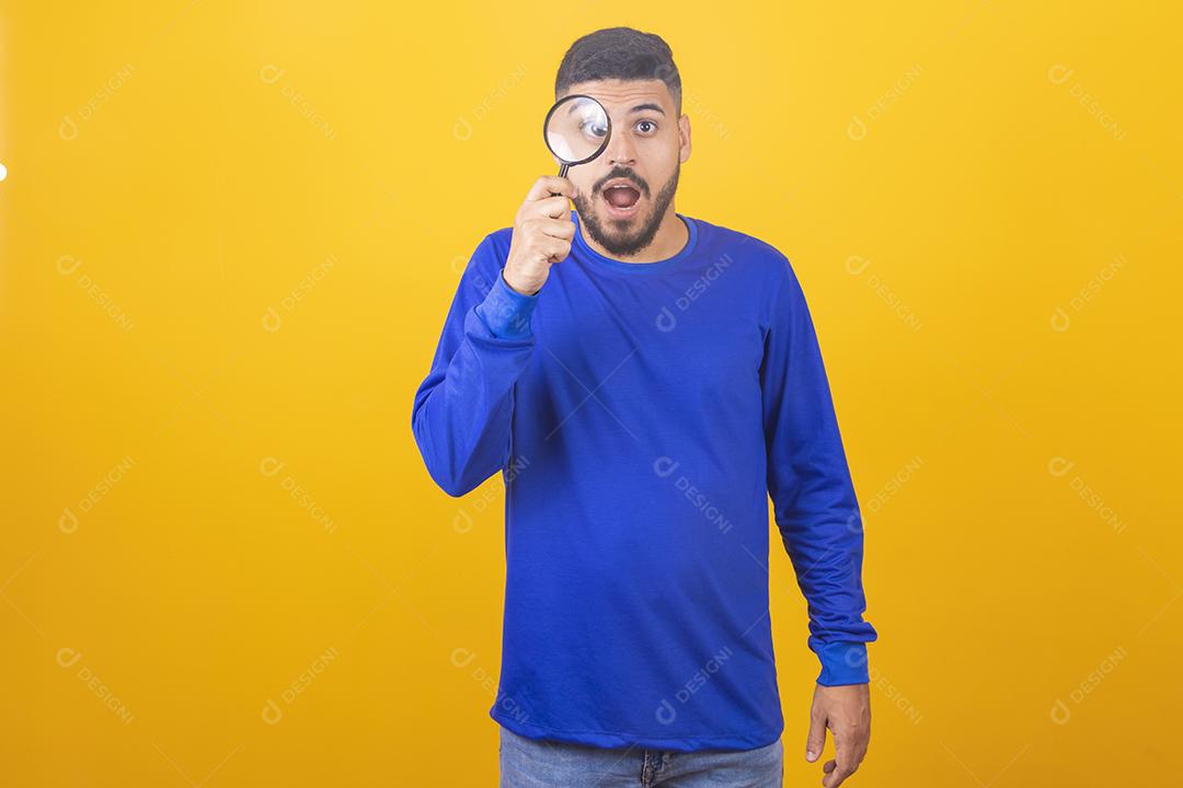 jovem detetive masculino segurando a lupa pelo olho direito em pé na frente da câmera em isolamento