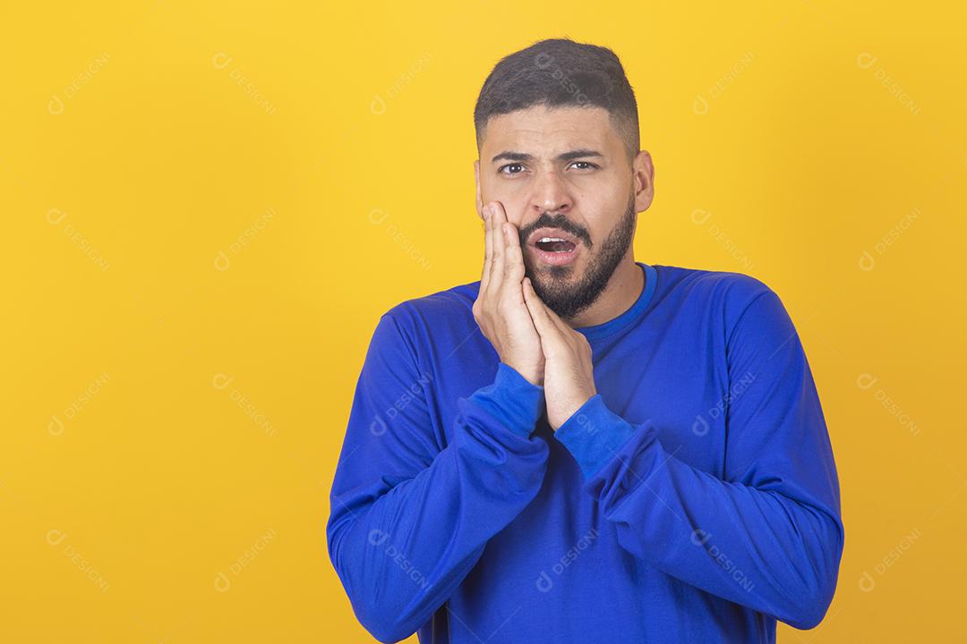 Dor de dente. Jovem sentindo dor, segurando a bochecha com as duas mãos, sofrendo de dor de dente, tendo expressão dolorosa