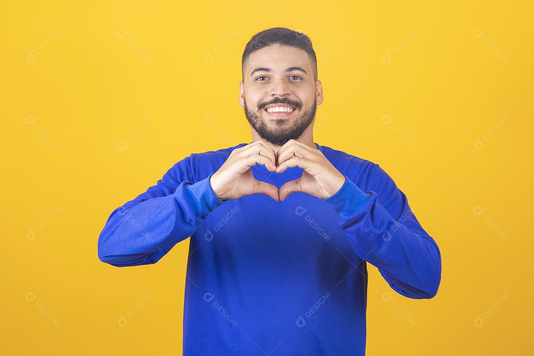 Retrato de jovem sorridente mantém as mãos no peito em sinal de forma de coração, expressa simpatia.
