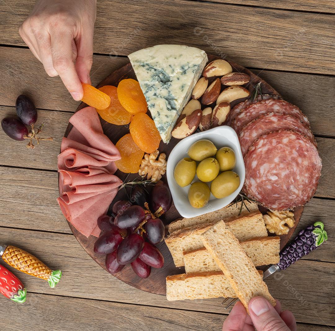 Pessoas pegando comida da tábua de aperitivos com queijo, nozes, frutas