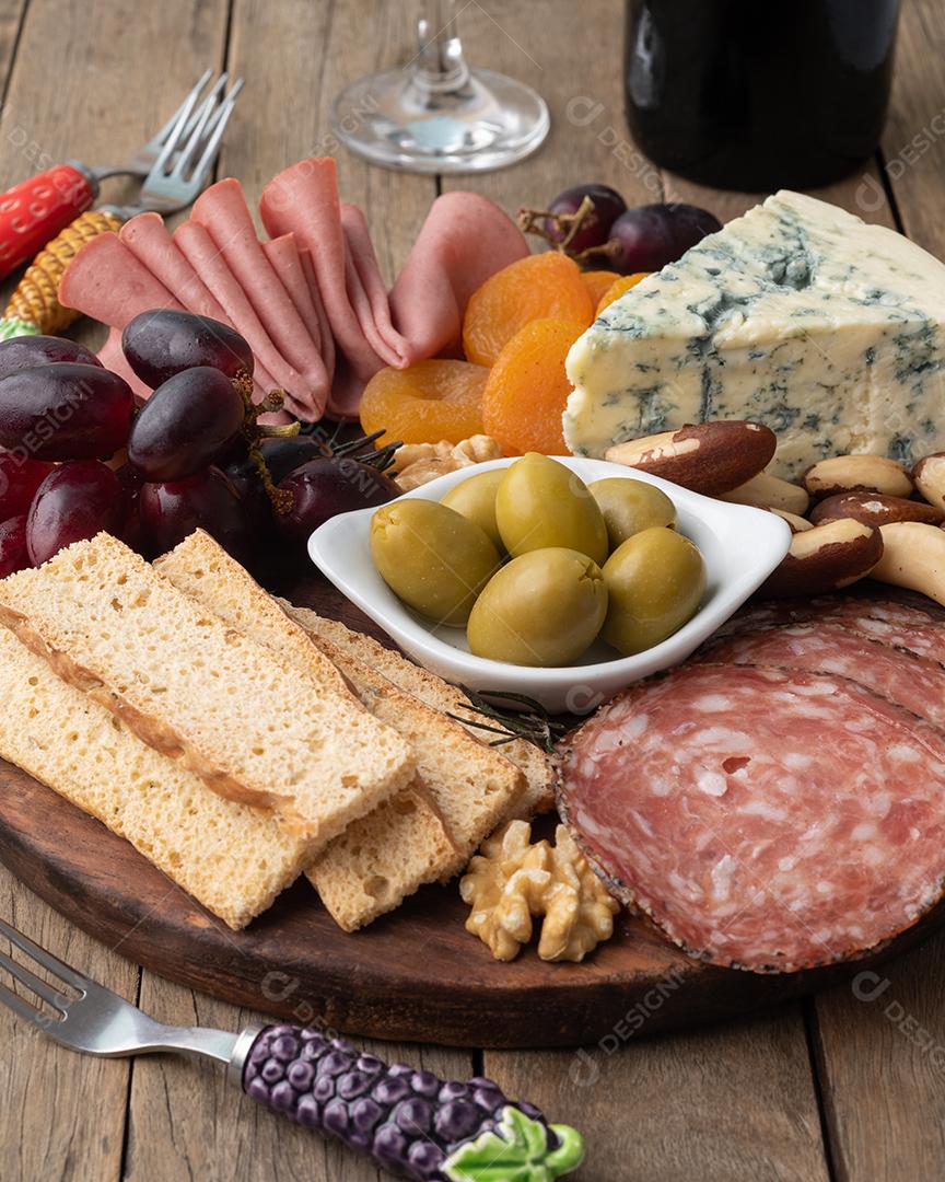 10404434aTábua de aperitivos com queijo, nozes, frutas, torradas, vinho e charcutaria sobre a mesa de madeira.