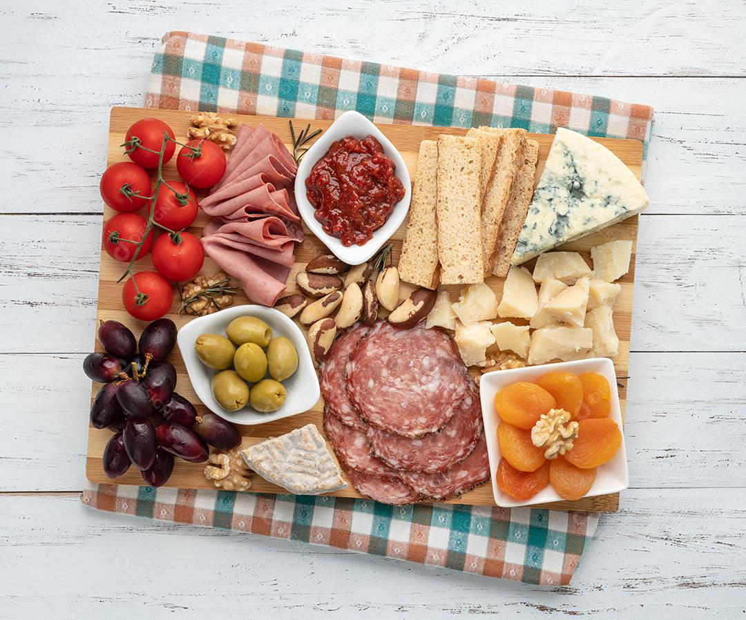 Tábua de aperitivos com queijo, nozes, frutas, torradas e embutidos isolados sobre fundo branco.