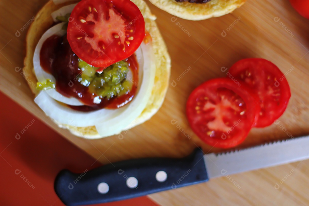 Hambúrgueres estão sendo preparados e servidos em tábuas de madeira, vista superior.