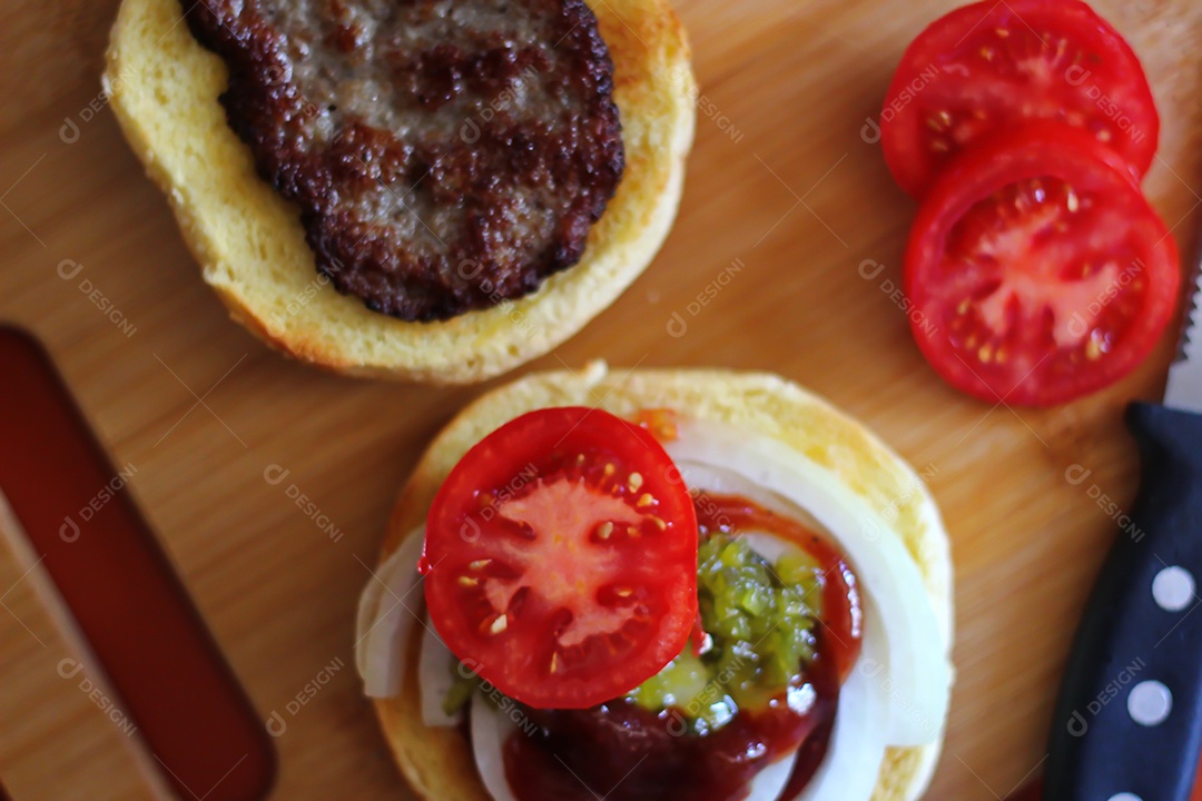 Hambúrgueres estão sendo preparados e servidos em tábuas de madeira, vista superior.