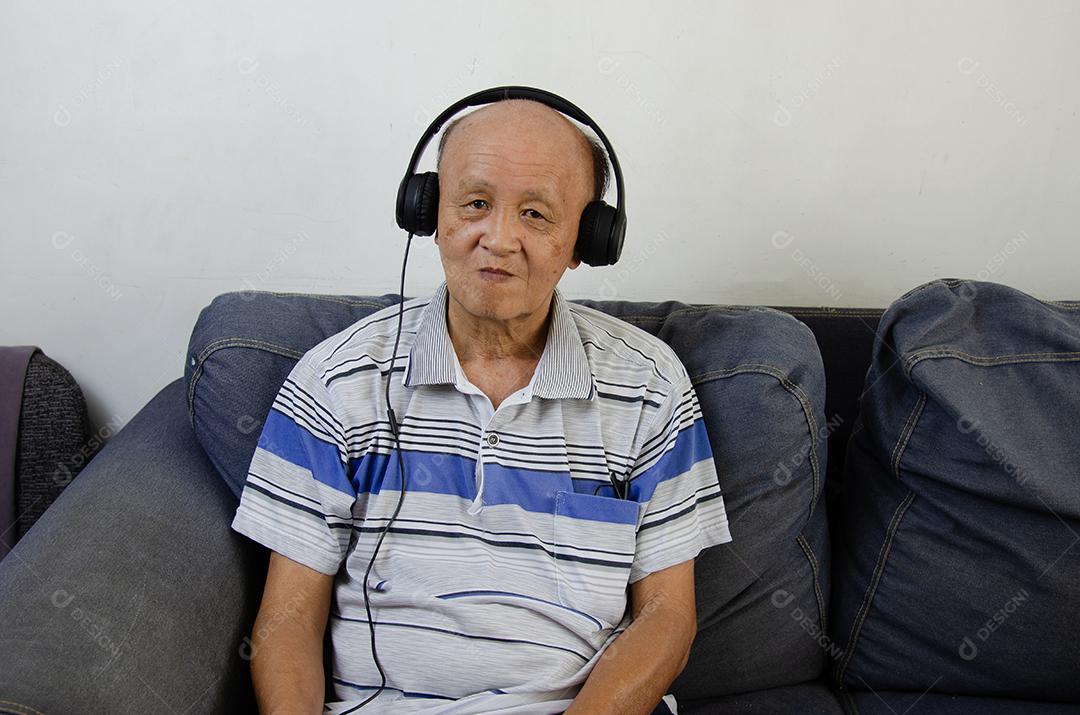 Homem idoso ouvindo música com fones de ouvido no sofá.