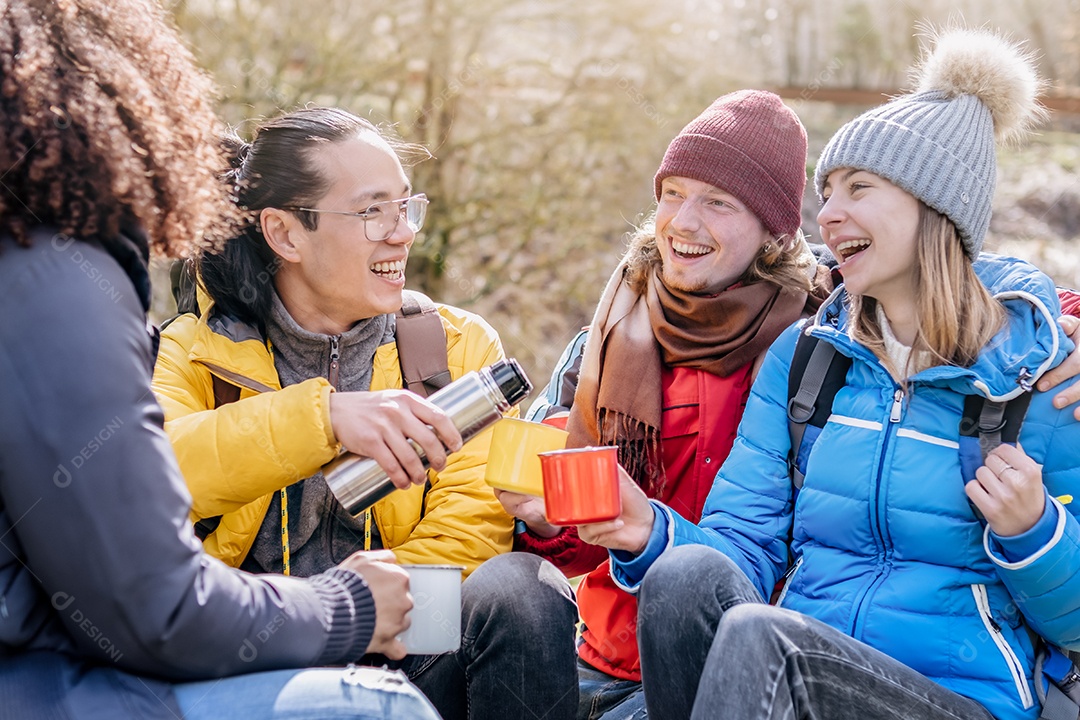 Grupo multicultural de caminhantes sentados no topo da montanha bebendo café com mochilas - Amigos