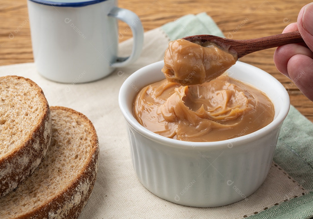 Mão recebendo doce de leite, doce de leite cremoso tradicional brasileiro com pão e café sobre a mesa de madeira.