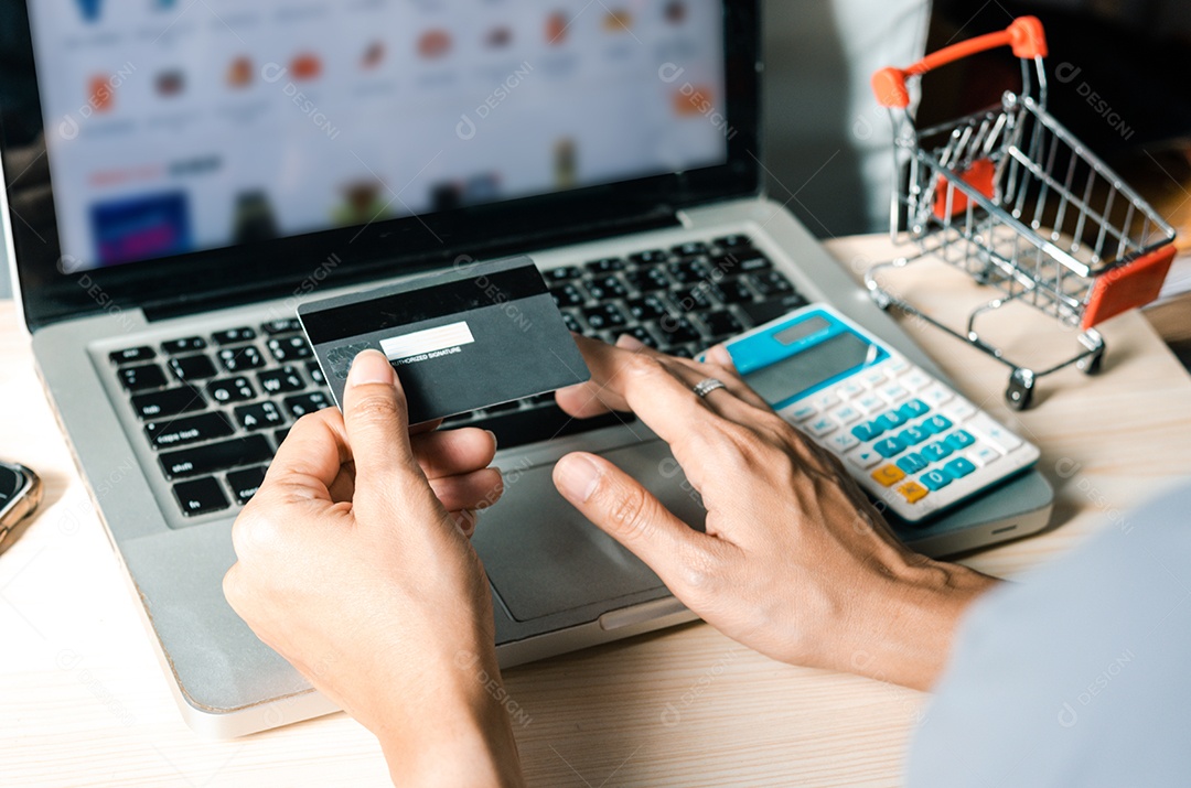 Mãos segurando um cartão de crédito e usando um laptop em cima da mesa