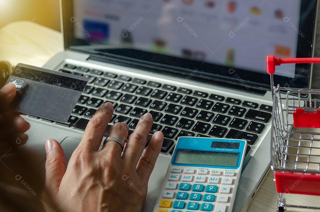 Mãos segurando um cartão de crédito e usando um laptop em cima da mesa
