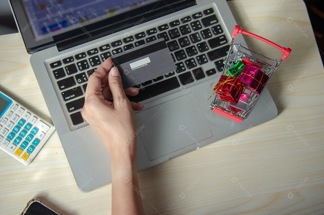 Mãos segurando um cartão de crédito e usando um laptop em cima da mesa