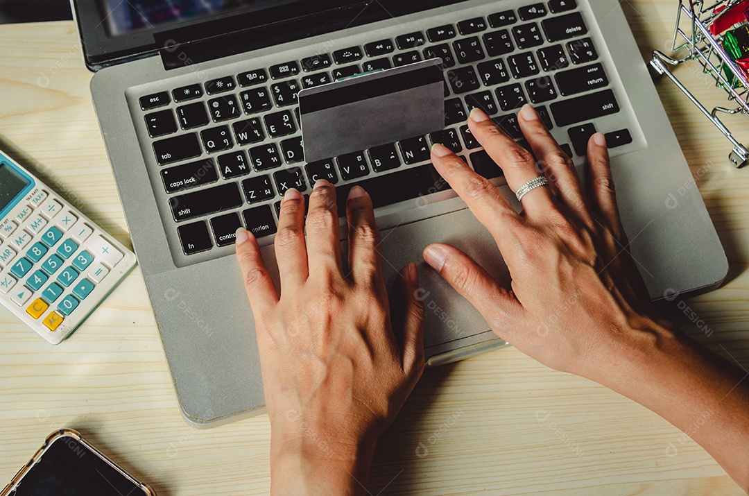 Mãos segurando um cartão de crédito e usando um laptop em cima da mesa