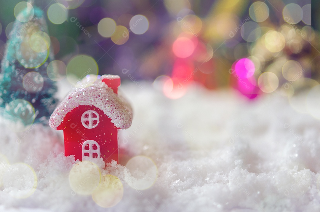 Casa vermelha e árvore de Natal na neve com bokeh de fundo.