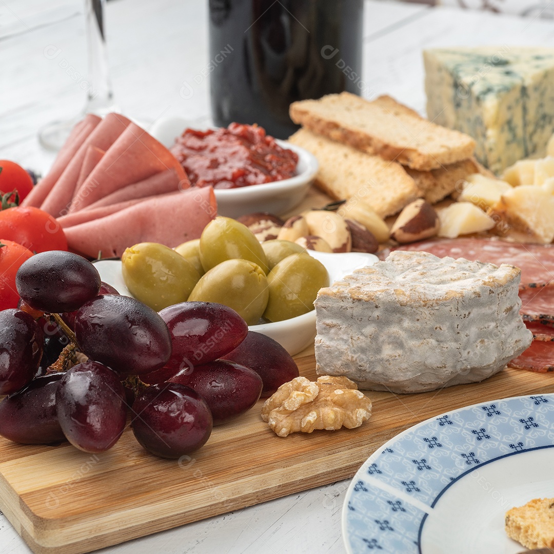 Tábua de aperitivos com queijo, nozes, frutas, torradas e charcutaria sobre a mesa de madeira.