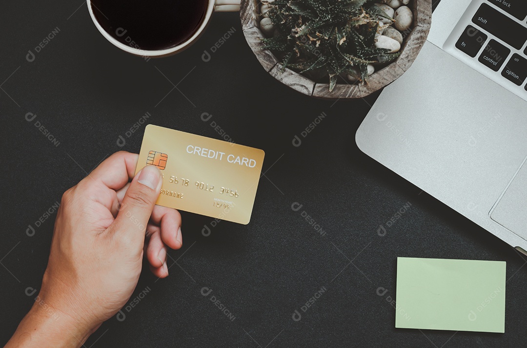 Homem de vista superior segurando um cartão de crédito e na mesa. Bloco de notas e caneta do computador portátil Negócios de compras online