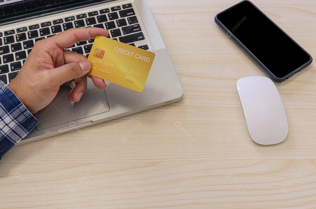 Mãos segurando um cartão de crédito e usando um laptop em cima da mesa