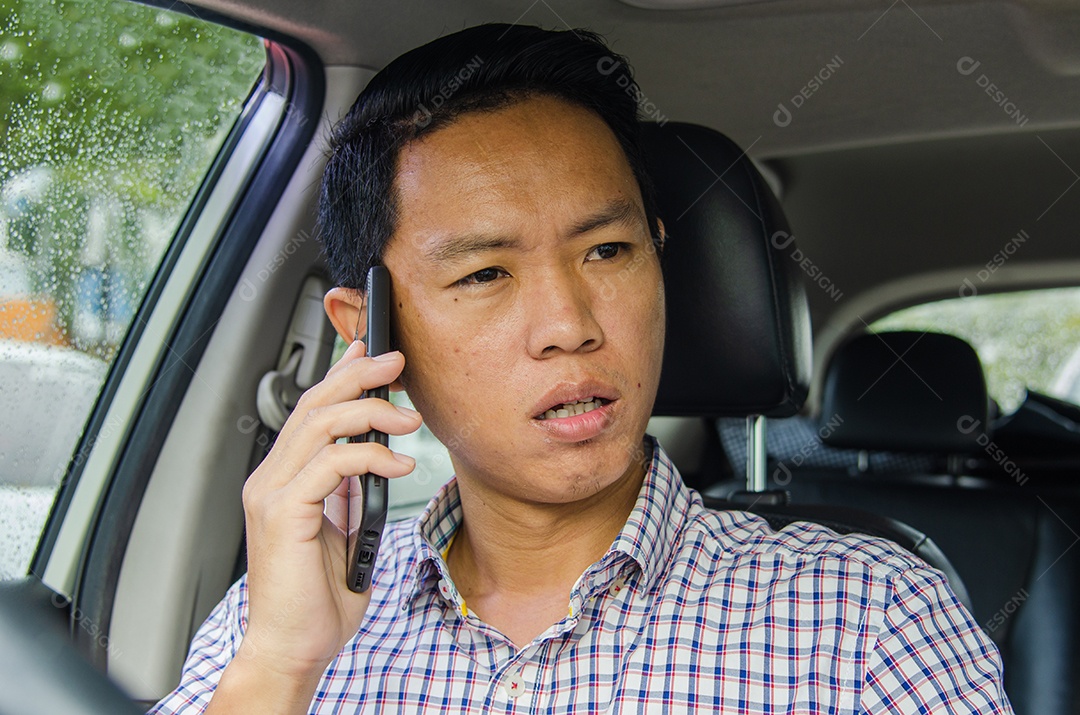 Homem asiático vestindo uma camisa xadrez olha para o telefone inteligente em um carro.