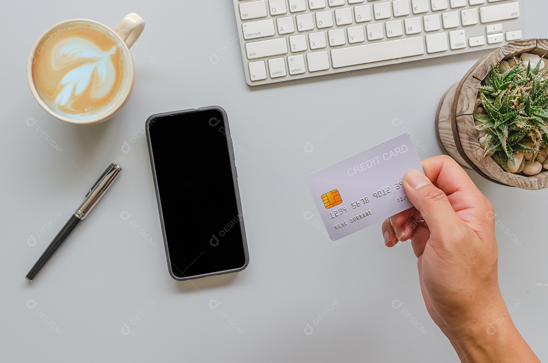 Homem de vista superior segurando um cartão de crédito na mesa. computador, café, caneta e smartphone. Negócios de compras online, pague com cartão de crédito