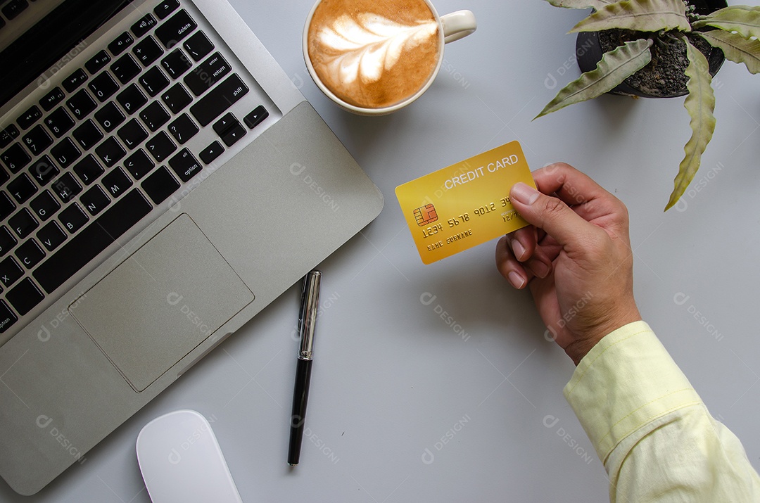 Homem de vista superior segurando um cartão de crédito e na mesa. Bloco de notas e caneta do computador portátil Negócios de compras online, pague com cartão de crédito