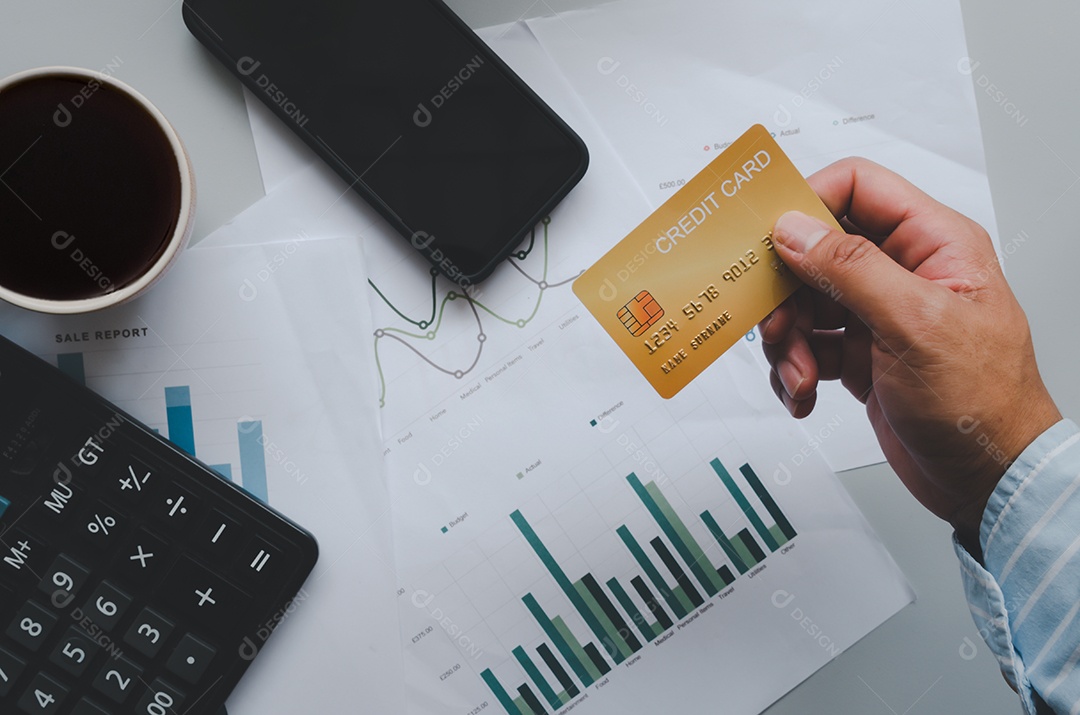 Homem de vista superior segurando um cartão de crédito e na mesa. Calculadora de documentos de negócios e caneca de café e smartphone. Negócios de compras on-line, pague com cartão de crédito.