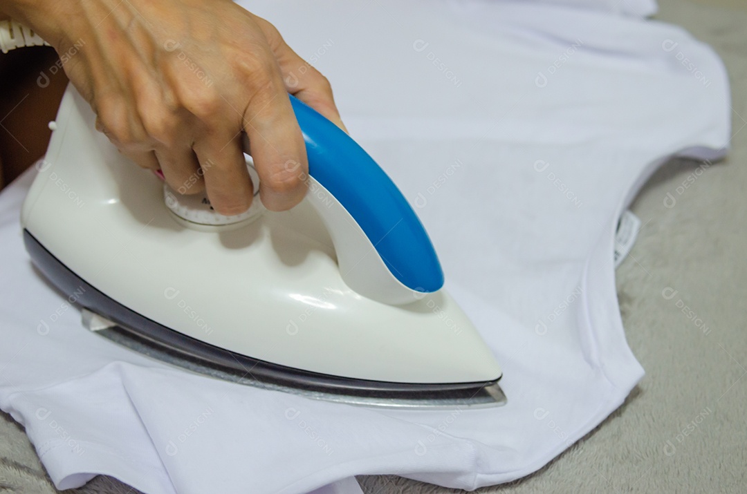 Mão de uma mulher segurando o ferro. Passando a camisa branca