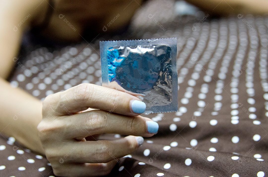 Mão de mulher com pacote de preservativo na cama.