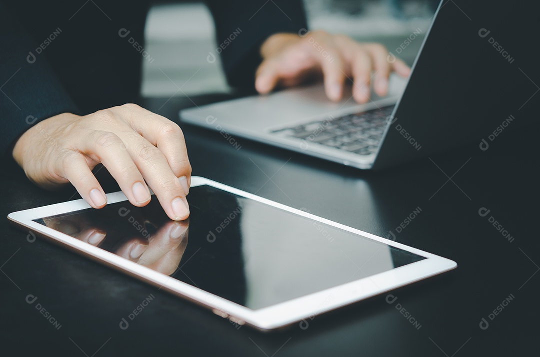 Empresário com um tablet de toque e um computador portátil procura informações com tecnologia de Internet trabalhando na mesa.