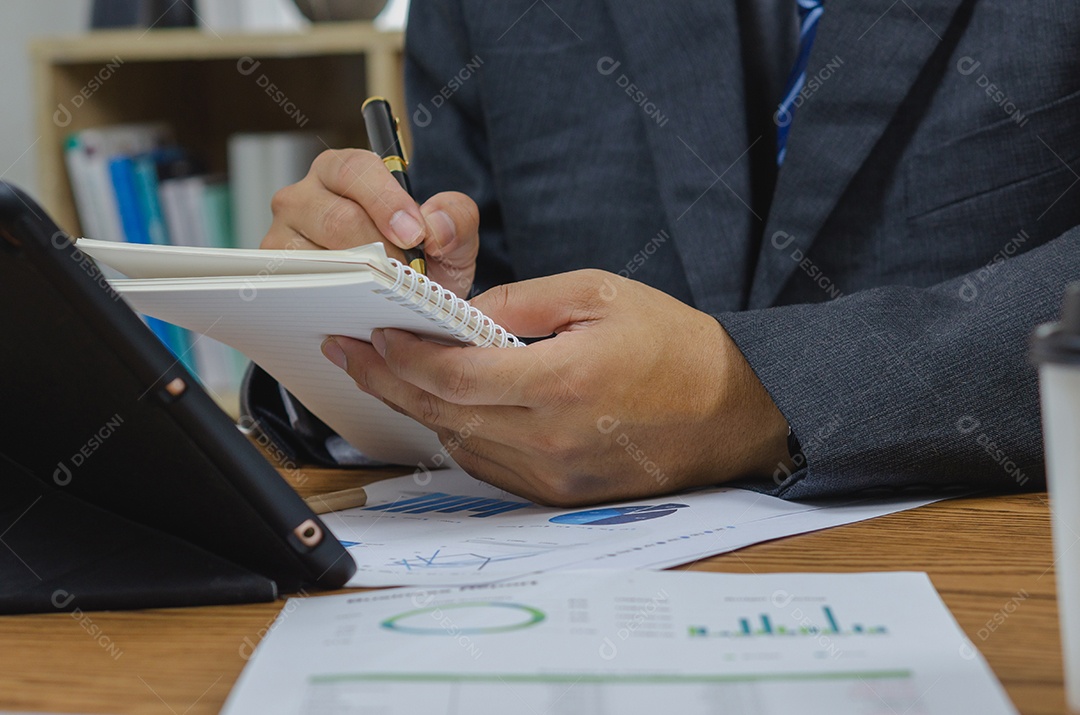 Empresário segurando o gráfico de documento de caneta contabilidade finanças papel análise gráfico investimento de marketing e economia de relatório com computador portátil na mesa no escritório.