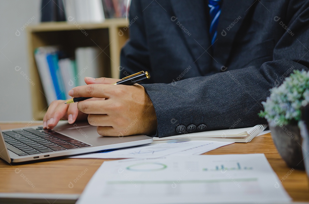 Empresário segurando o gráfico de documento de caneta contabilidade finanças papel análise gráfico investimento de marketing e economia de relatório com computador portátil na mesa no escritório.