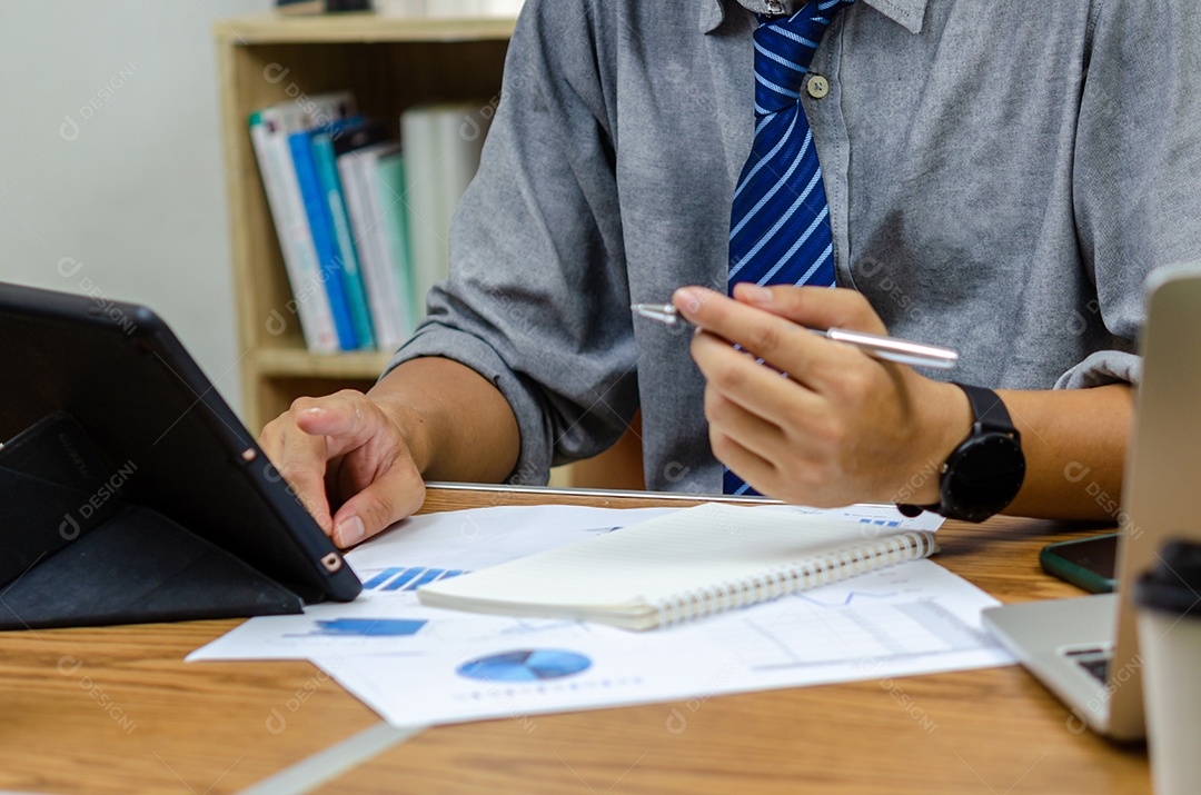 Empresário segurando o gráfico de documento de caneta contabilidade finanças papel análise gráfico investimento de marketing e economia de relatório com computador portátil na mesa no escritório.