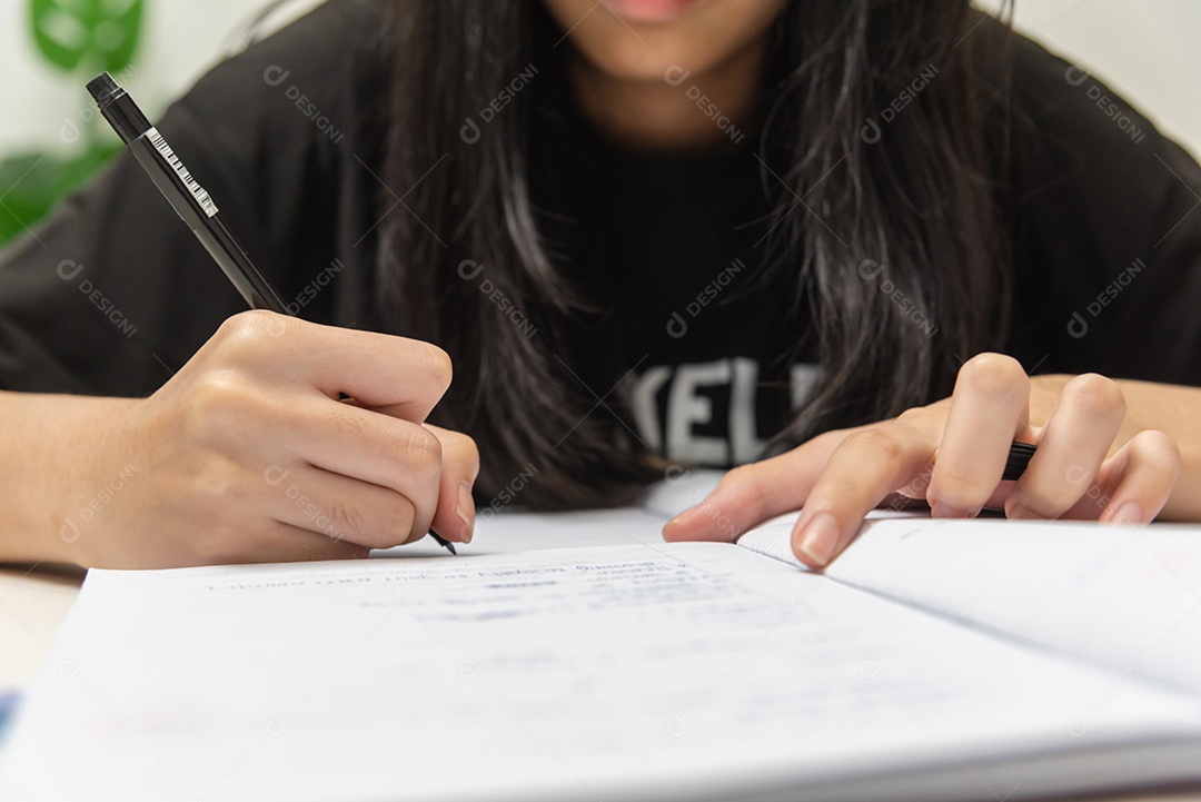 Aluna asiática está escrevendo lição de casa e lendo livro na mesa